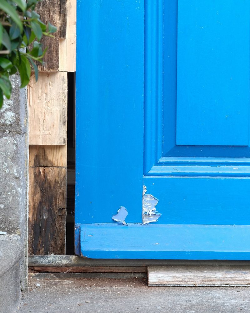 Foot of a door frame beside a blue door, the timber rotten and black