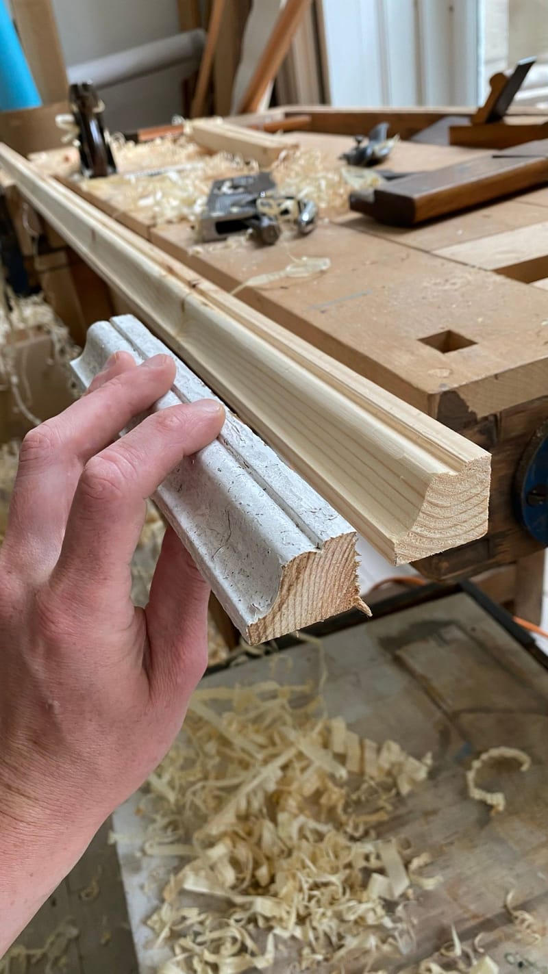 Old painted timber moulding held against a new length being shaped at the workbench