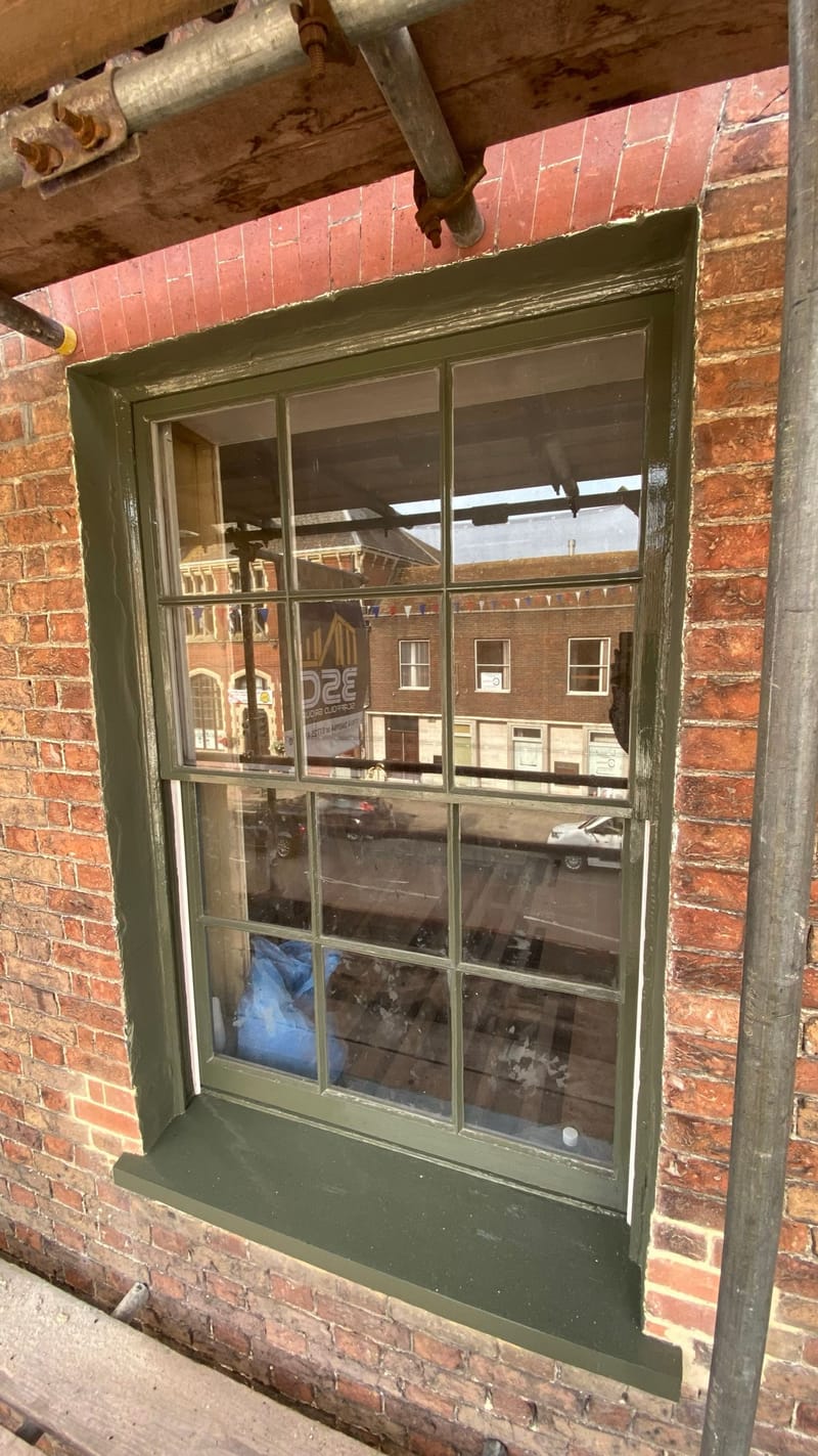 Restored timber sash window painted green, set in an old red brick wall